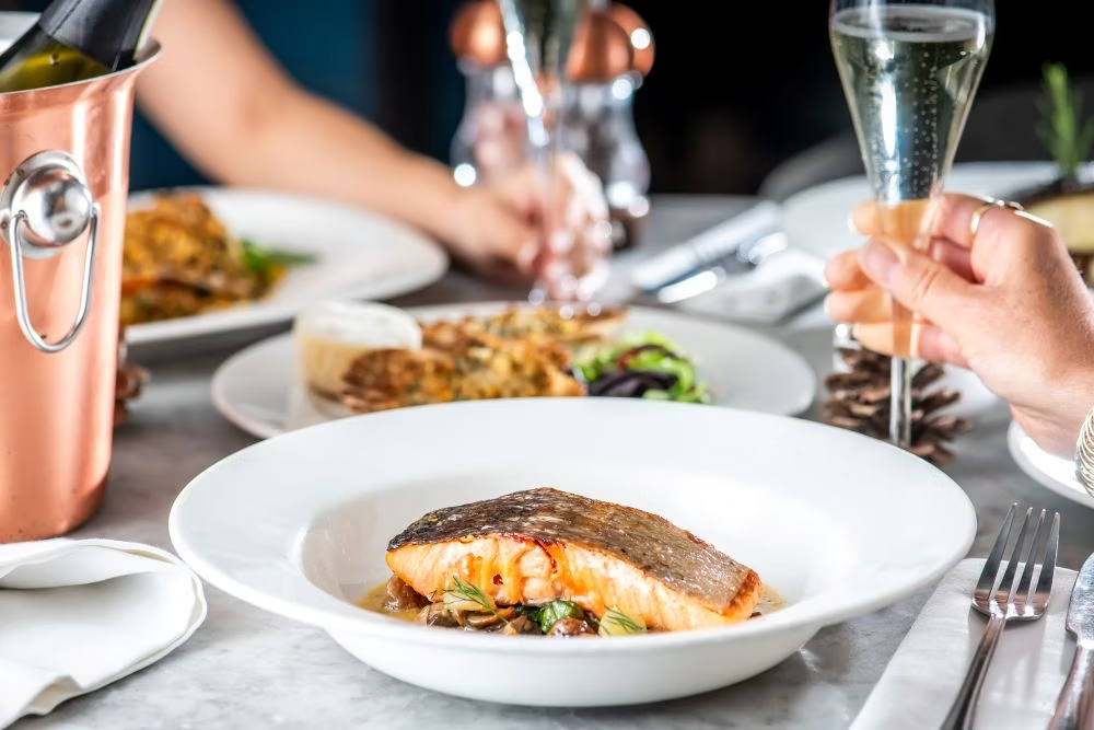 A plate of fried fish and someone holding a glass of sparkling wine at FishWorks