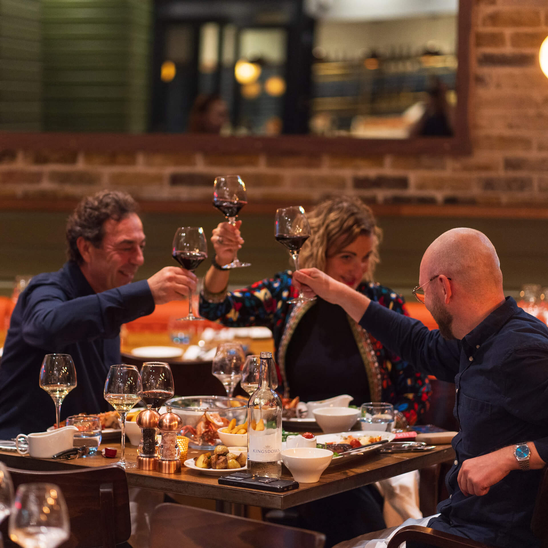 A group of two men and a woman raising red wine glasses at Fishworks private dining